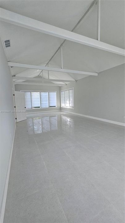 Vaulted ceiling with exposed structural beams, large format light-toned tile flooring, and multiple windows with white horizontal blinds