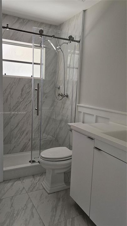 Walk-in shower with sliding glass door, stone-finish wall tile, white vanity with integrated sink, and wainscoting detail