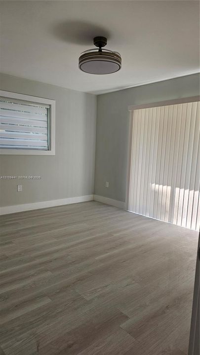 Neutral wall tones, wood-finish flooring, ceiling-mounted light fixture, sliding glass door with vertical blinds, and window with horizontal blinds