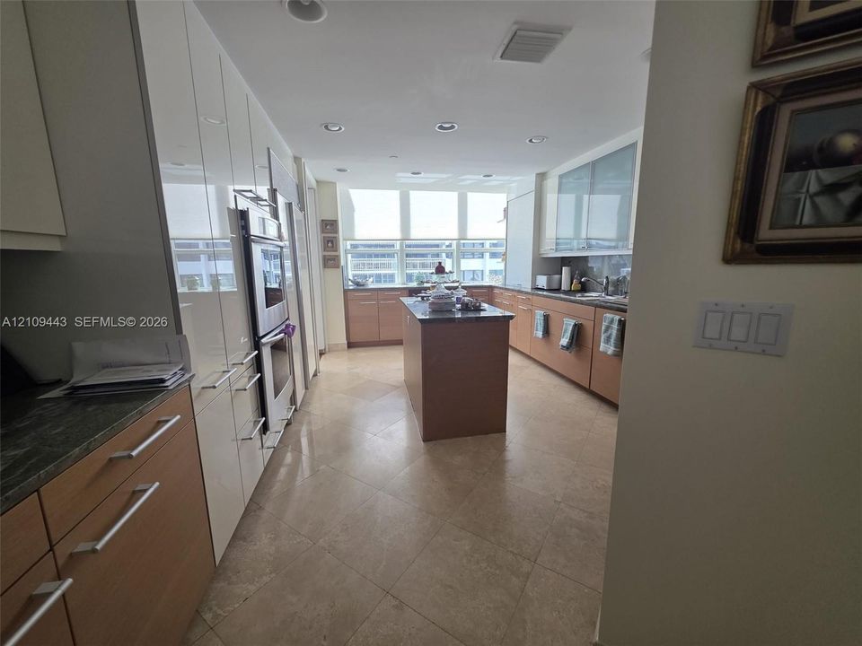 Kitchen featuring two-tone cabinetry with wood-finish lower units and high-gloss upper cabinetry, stone countertops, a central kitchen island, and large-format tile flooring