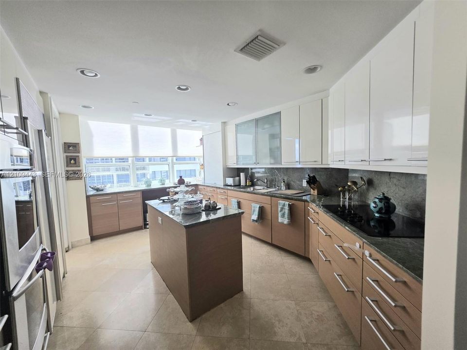 Kitchen featuring two-tone cabinetry, central island, stone-finish countertops, tile flooring, and integrated stainless steel wall oven