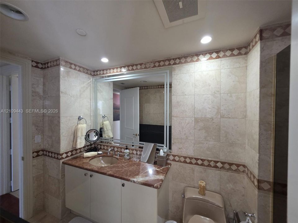 Vanity featuring a stone countertop with an integrated basin, neutral tile wall cladding, and decorative diamond-patterned tile inlay
