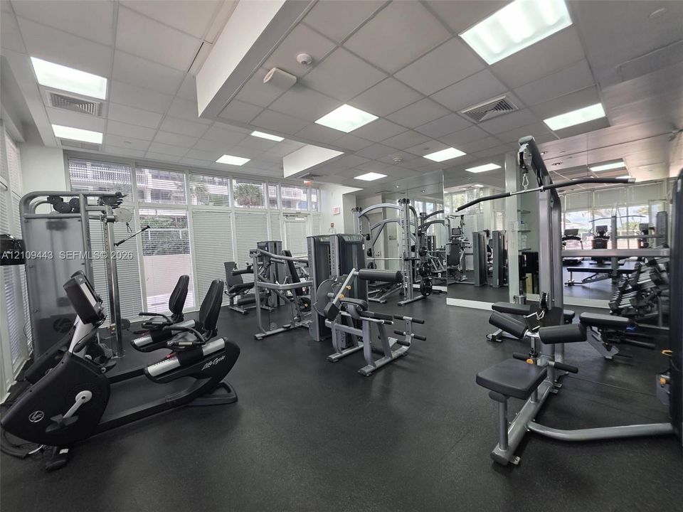 Fitness center featuring recessed square lighting, wall-to-wall mirrors, rubberized flooring, and expansive windows