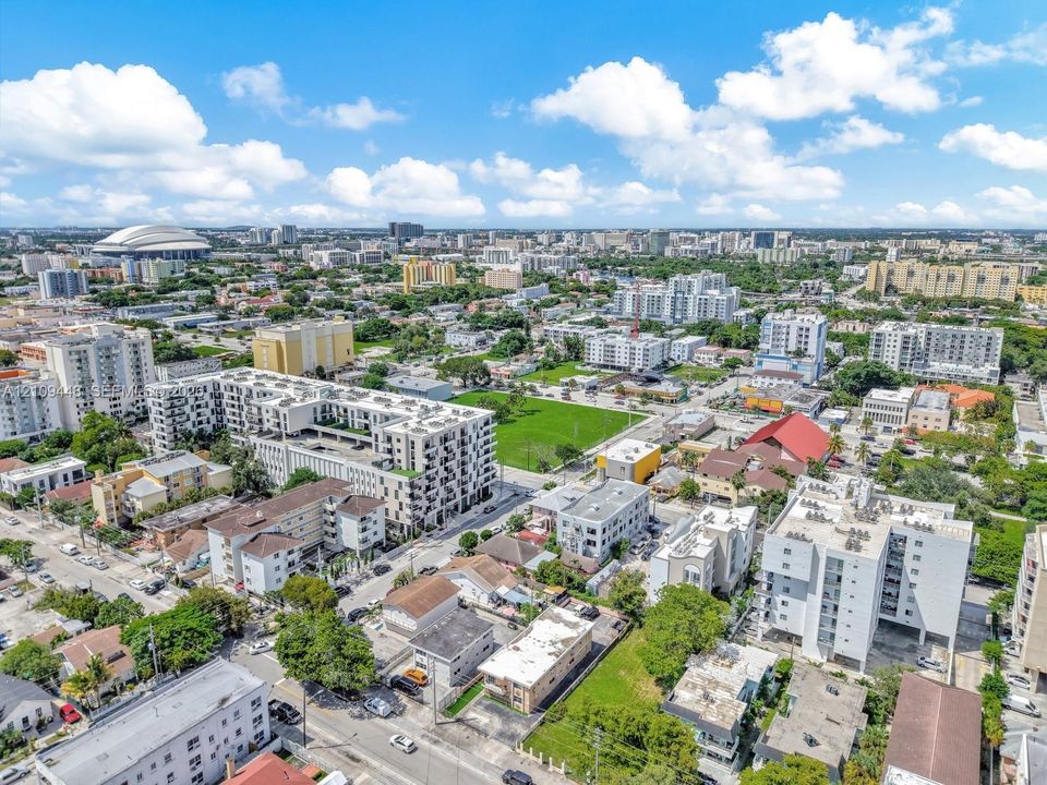 Aerial perspective of a high-density urban environment featuring multi-story residential buildings, paved street grids, landscaped green spaces, and surrounding metropolitan infrastructure