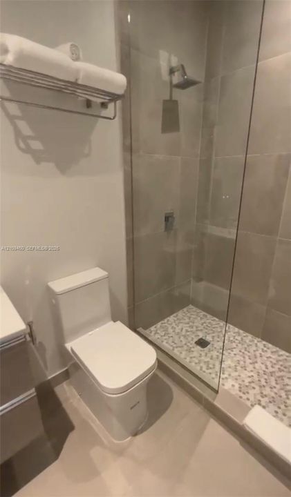 Glass-enclosed shower with pebble tile flooring, wall-mounted rainfall showerhead, and polished chrome fixtures
