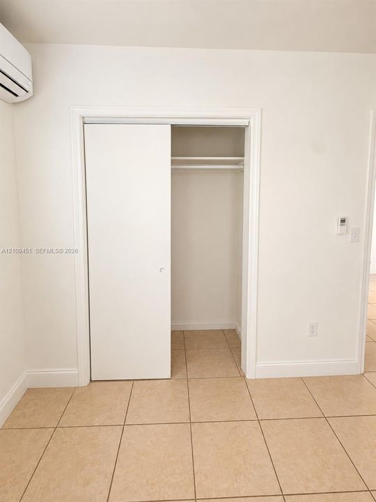 Closet featuring a sliding door and an integrated overhead shelf with hanging rod, accompanied by neutral tile flooring and a wall-mounted climate control unit