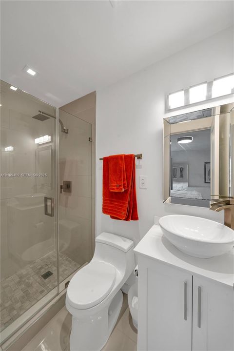 Glass-enclosed shower with stone-tile flooring, white vanity cabinet, countertop vessel sink, and wall-mounted vanity light fixture
