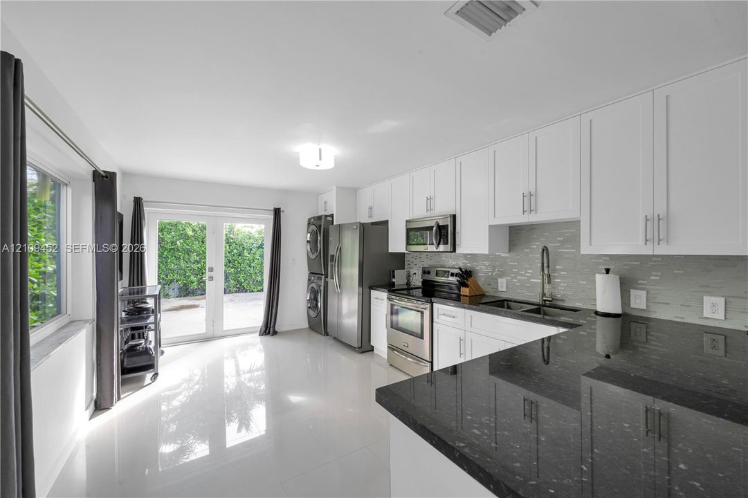 Kitchen featuring white cabinetry, dark stone countertops, stainless steel appliances, multi-toned horizontal tile backsplash, and glass-paneled double doors