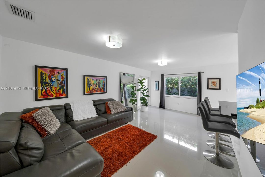Interior space featuring polished tile flooring, dual flush-mount ceiling light fixtures, and a large picture window with neutral drapery