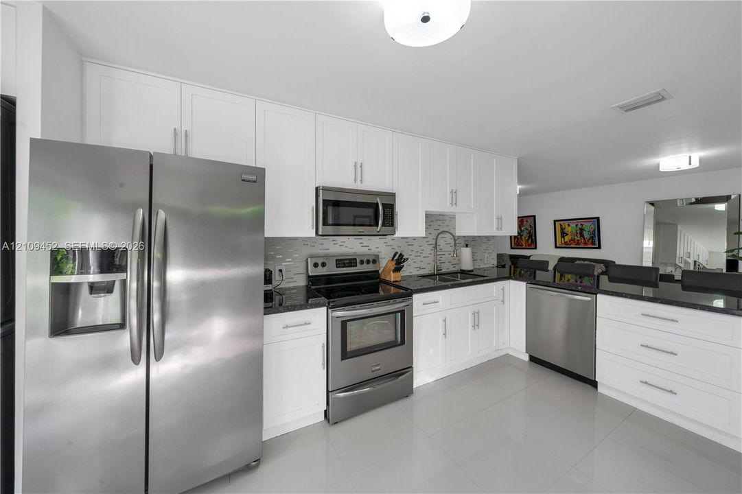 Kitchen featuring white shaker-style cabinetry, dark stone countertops, a tiled backsplash, and stainless steel appliances including a side-by-side refrigerator, over-the-range microwave, and electric range