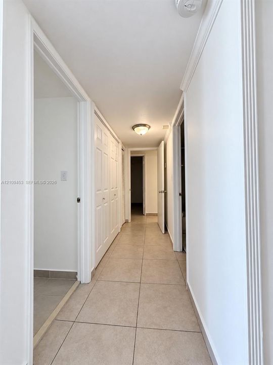 Hallway featuring large-format ceramic tile flooring, multi-panel doors, decorative door casing, and a flush-mount ceiling light fixture