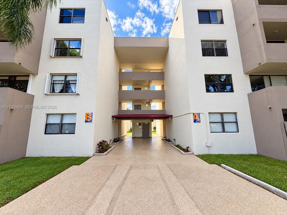 Multi-story exterior facade featuring light-toned stucco, multiple levels of private balconies, and a paved central entryway