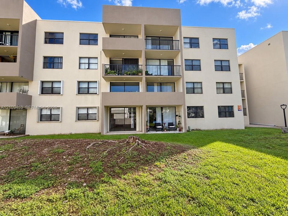 Multi-story stucco building exterior featuring private recessed balconies, sliding glass door access, metal railings, and expansive grass landscaping