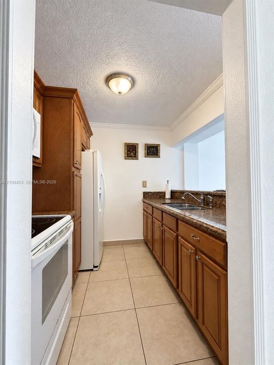 Kitchen featuring wood cabinetry, stone-finish countertops, ceramic tile flooring, a dual-basin stainless steel sink, and crown molding