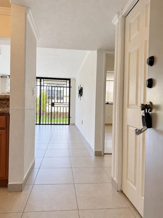 Entryway featuring large-format neutral floor tile, crown molding, and a metal security gate door