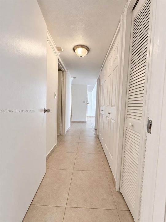 Neutral-toned tile flooring, flush-mount lighting, and floor-to-ceiling closets featuring paneled and louvered doors