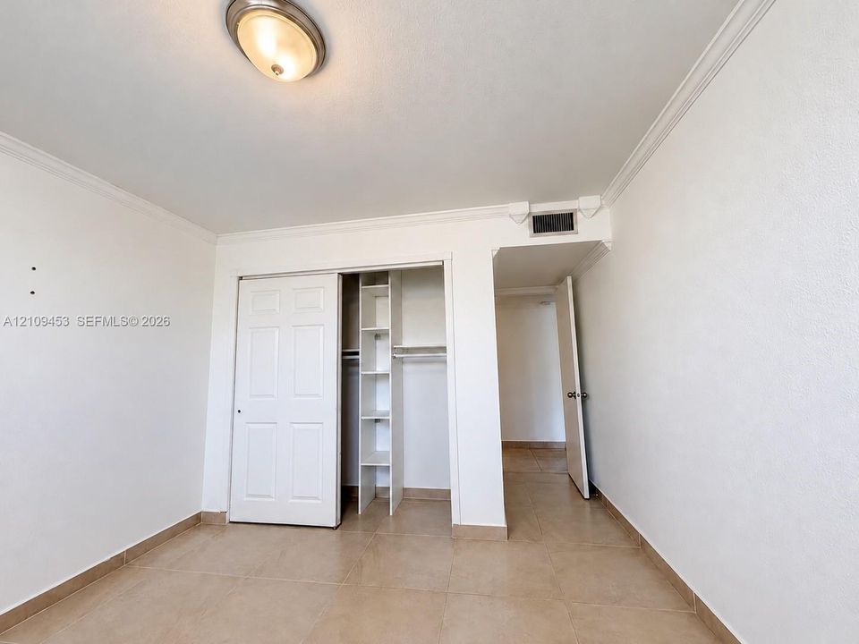 Room featuring neutral tile flooring, crown molding, a semi-flush mount ceiling light, and a reach-in closet with integrated shelving