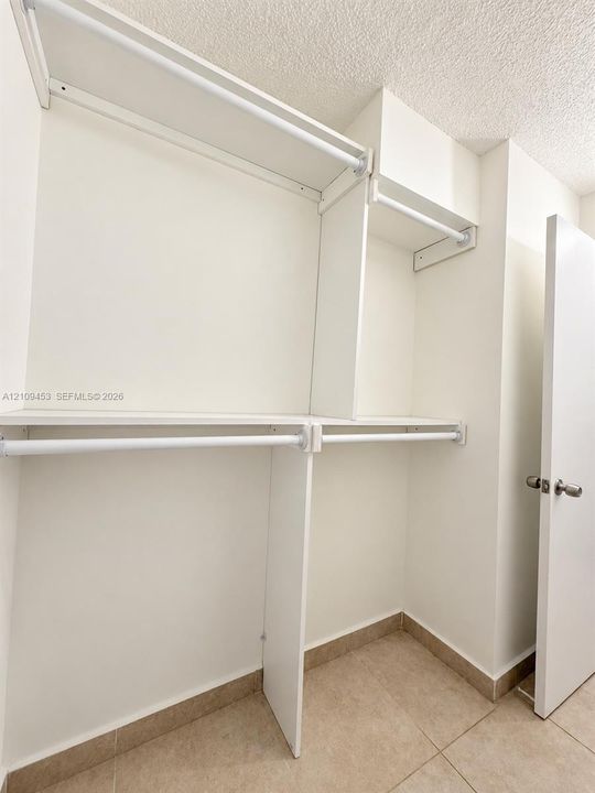 Built-in white shelving system featuring multiple storage tiers, integrated garment rods, white panel door with metal hardware, and tiled flooring