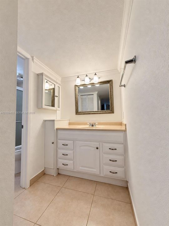 White vanity with integrated cabinetry and drawers, light-toned countertop, wall-mounted three-light fixture, and ceramic tile flooring