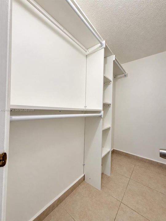Walk in Closet Built-in white storage system featuring integrated shelving and horizontal clothing rods, complemented by tile flooring