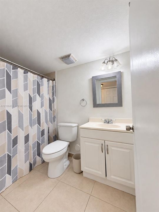 Bathroom featuring a white vanity with an integrated basin, a wall-mounted mirror with a grey frame, tile flooring, and a three-light fixture
