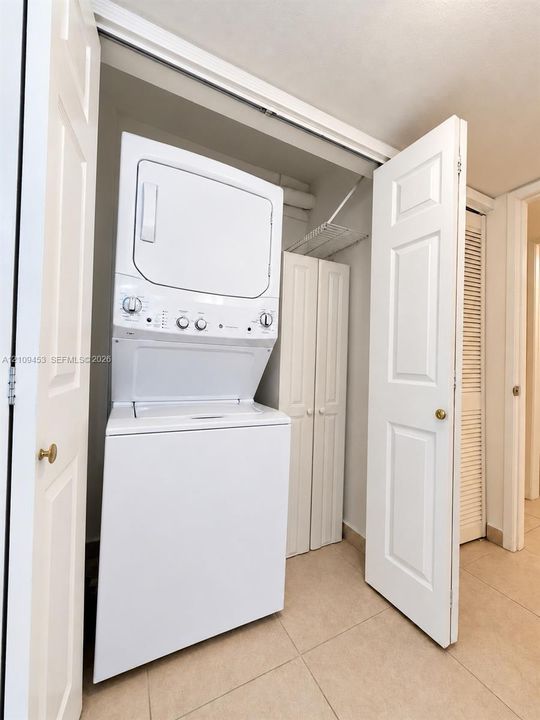 Laundry closet featuring a built-in stacked washer and dryer unit, custom panel-door cabinetry, and an overhead wire shelving system