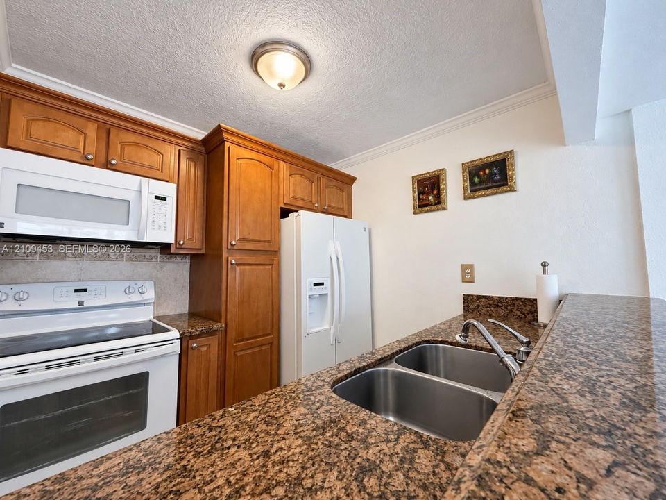 Kitchen featuring stained wood cabinetry, stone countertops, double-basin stainless steel sink with high-arc faucet, and white appliances