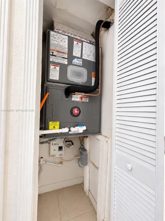 Wall-mounted HVAC unit with copper piping and integrated electrical components, housed within a closet featuring louvered bi-fold doors