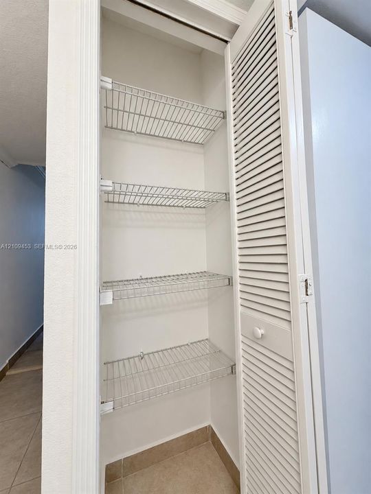 Tall storage closet featuring white louvered doors and four adjustable wire shelving tiers