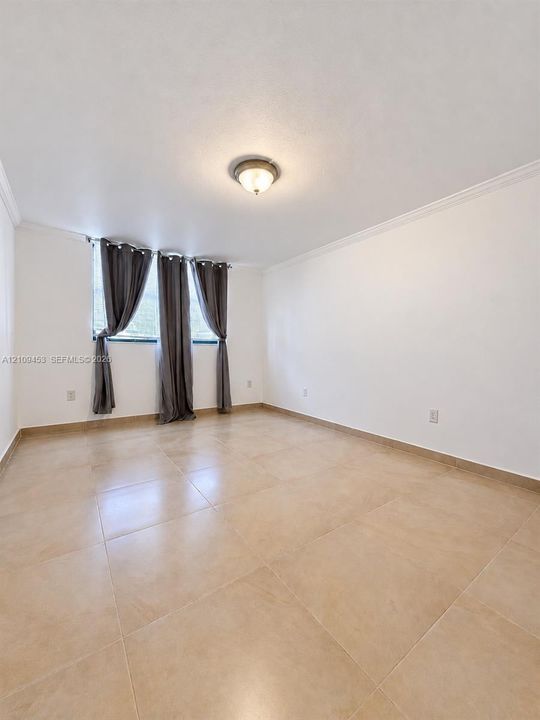 Room with large-format tile flooring, crown molding, and a central flush-mount ceiling light fixture