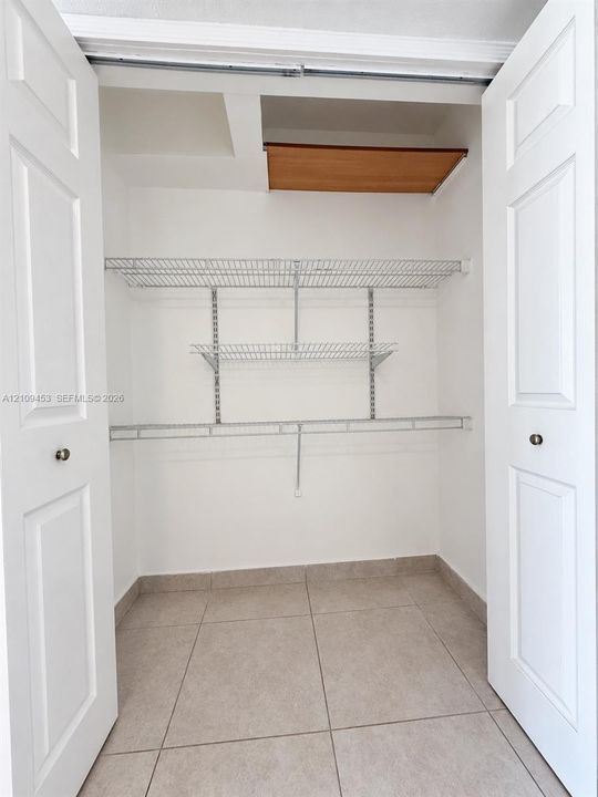 Storage closet featuring white paneled double doors, neutral tile flooring, and integrated white wire shelving