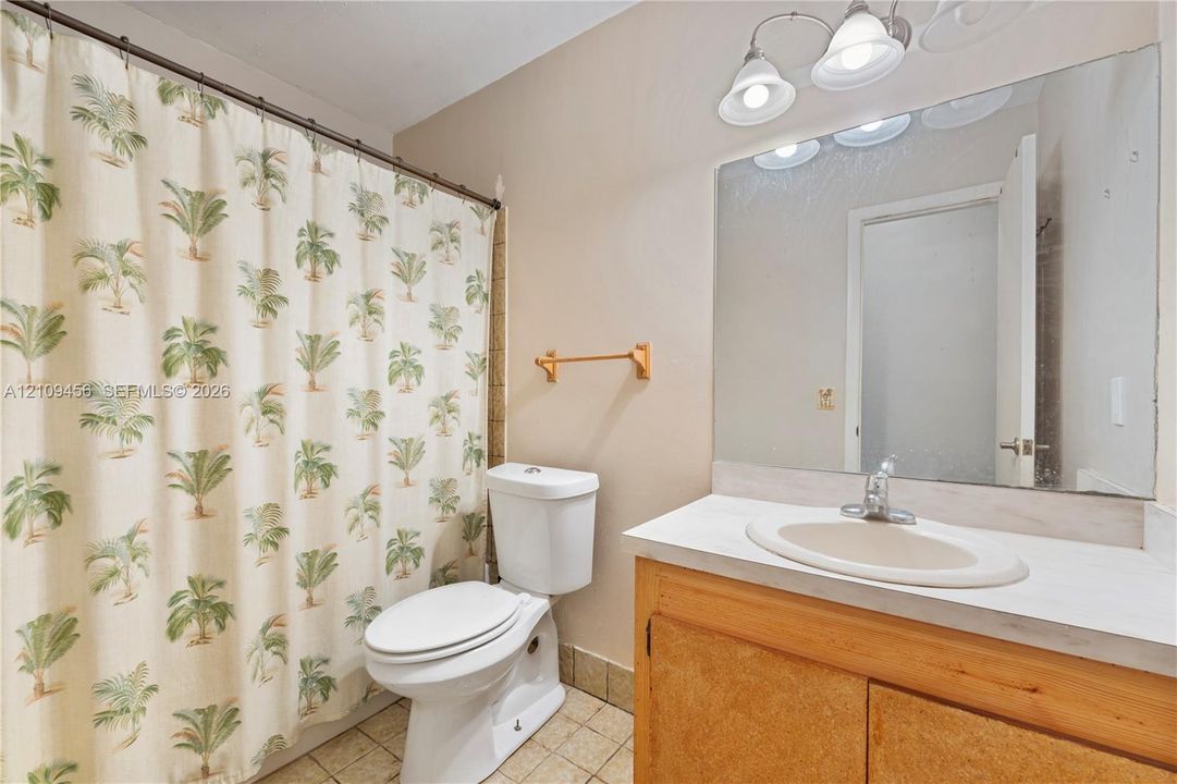 Bathroom featuring a wood-finish vanity with an integrated oval sink, a wall-spanning mirror, three-light vanity fixture, and tiled flooring