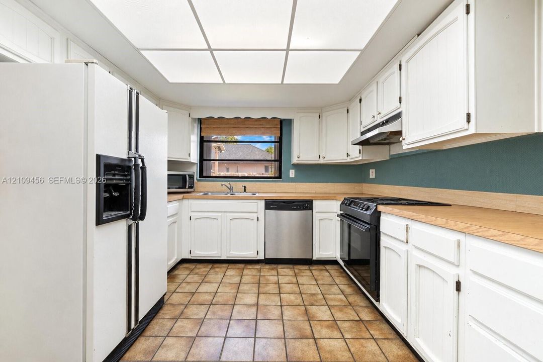 Kitchen featuring white cabinetry, light-toned countertops, ceramic tile flooring, a stainless steel dishwasher, and a recessed tray ceiling with integrated lighting