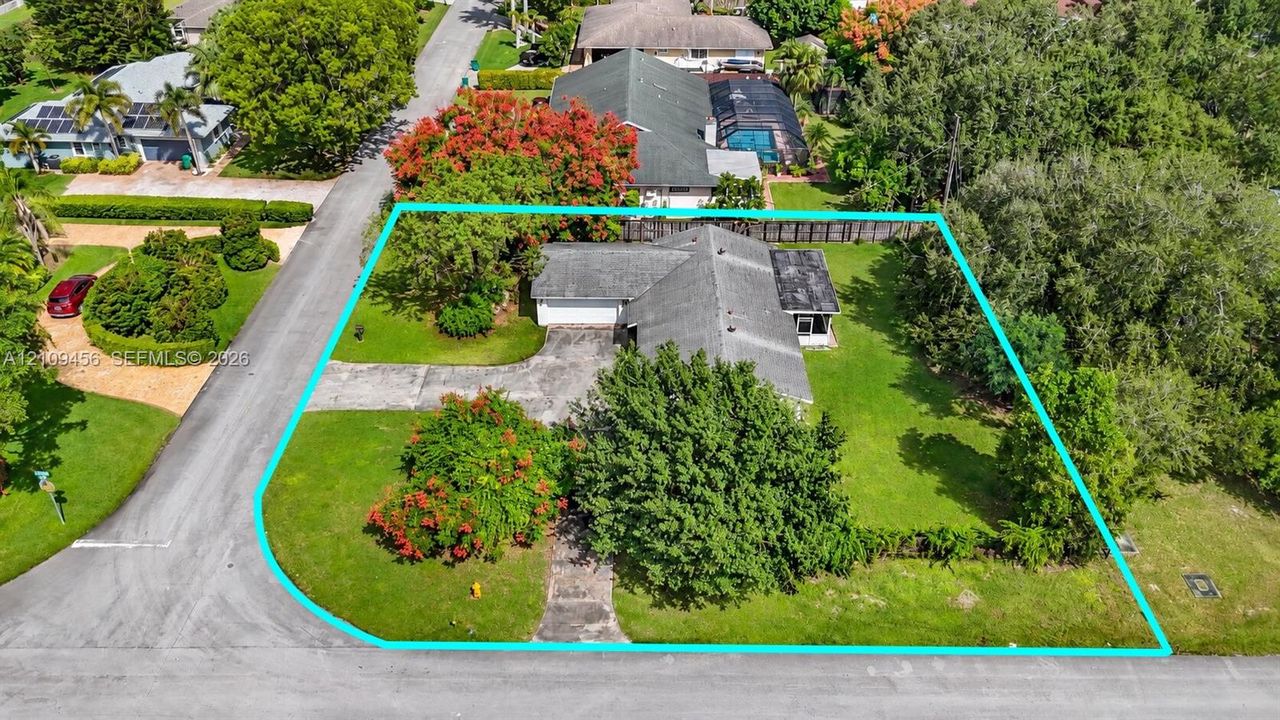 Corner lot featuring a concrete driveway, multi-gabled roofline, mature trees, and landscaping