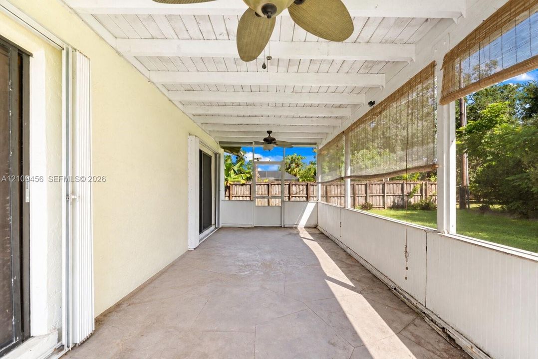Screened patio featuring a painted exposed-beam ceiling, two ceiling fans, concrete flooring, and sliding glass doors