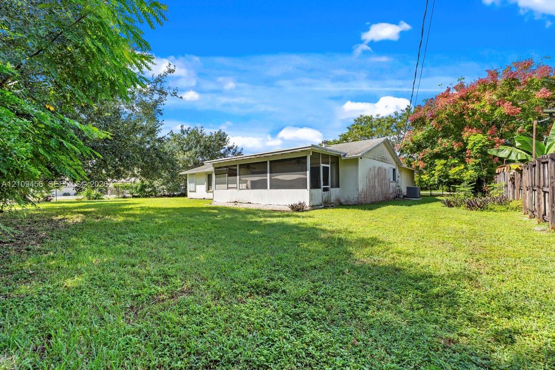Expansive backyard featuring a large grass lawn, mature trees, and a screened-in porch with a gabled roofline