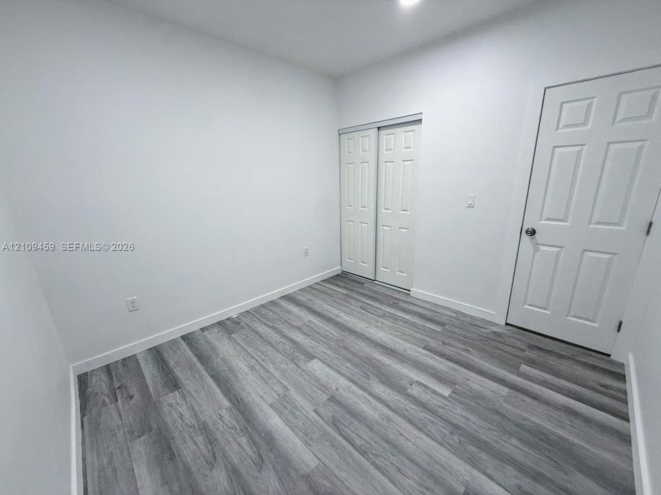 Room featuring neutral walls, wood-finish flooring, a six-panel entry door, and a built-in closet with double-panel sliding doors