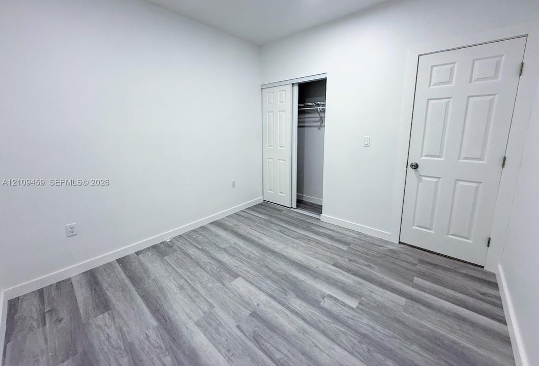 Neutral-toned wood-finish flooring, white walls, six-panel interior door, and a built-in sliding door closet