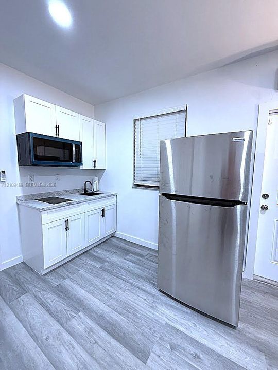 Kitchenette featuring white cabinetry, stone-patterned countertop, integrated stainless steel appliances, matte black faucet hardware, and wood-finish flooring