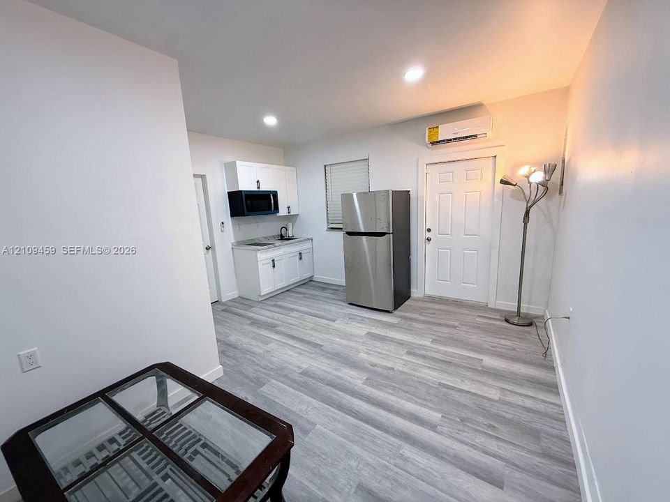 Kitchenette featuring white cabinetry, stainless steel refrigerator, microwave, and wood-finish flooring, complemented by a wall-mounted climate control unit