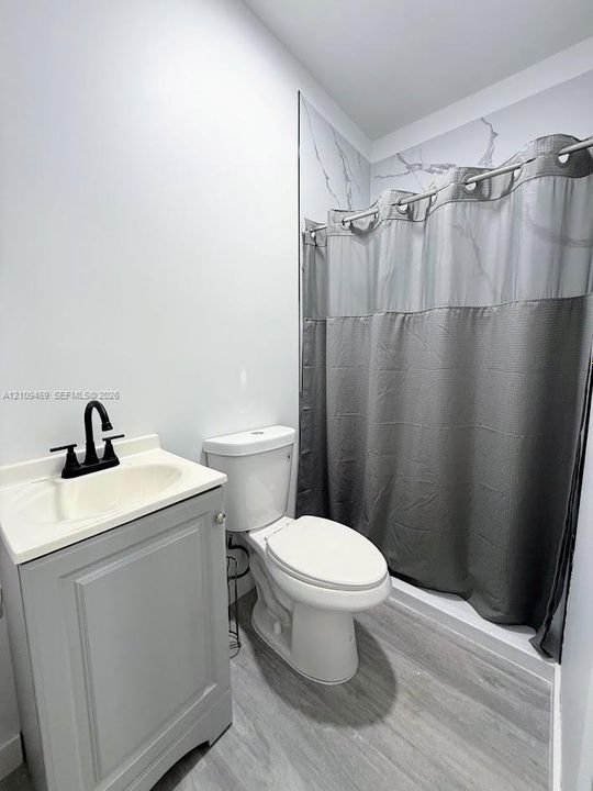 Bathroom featuring a grey shaker-style vanity, matte black faucet, and patterned wall surround in the tub area