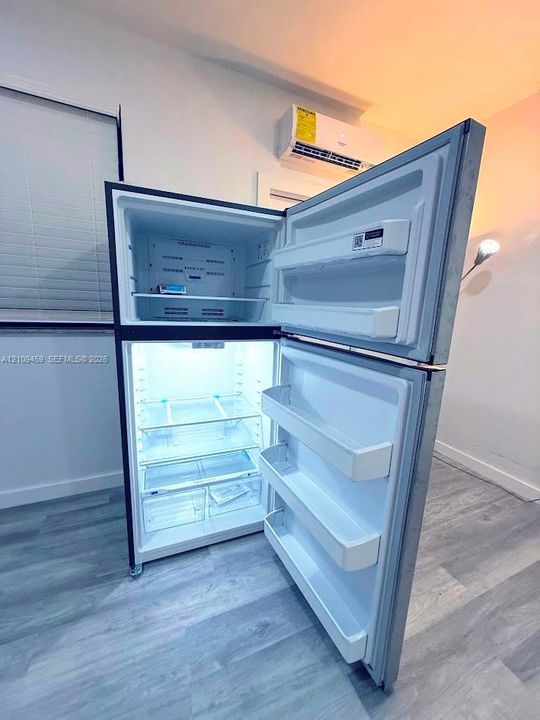 Top-mount stainless steel refrigerator with adjustable interior shelving and door storage, complemented by a wall-mounted ductless mini-split climate control system