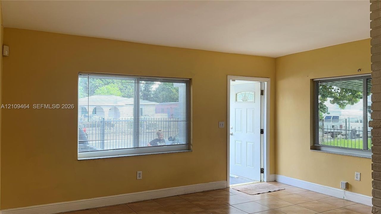Interior space featuring tile flooring, two horizontal sliding windows with blinds, a white-paneled exterior door, and exposed masonry pillar detailing