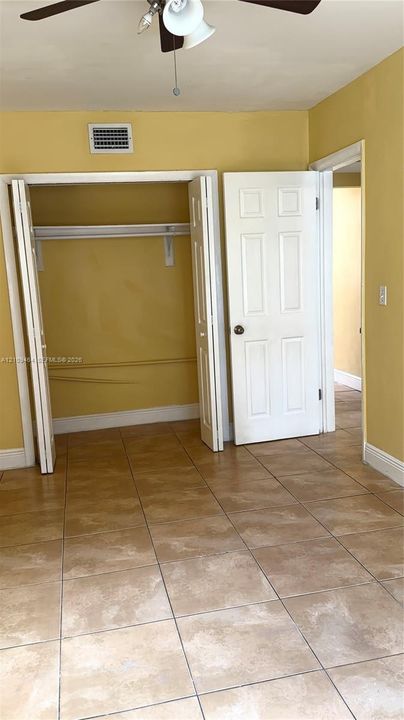 Tile flooring, bi-fold closet doors, interior six-panel door, and a ceiling-mounted fan/light
