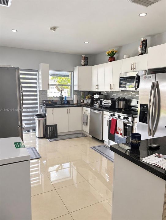 Kitchen featuring white cabinetry, polished dark countertops, stainless steel appliances, large-format tile flooring, and recessed lighting