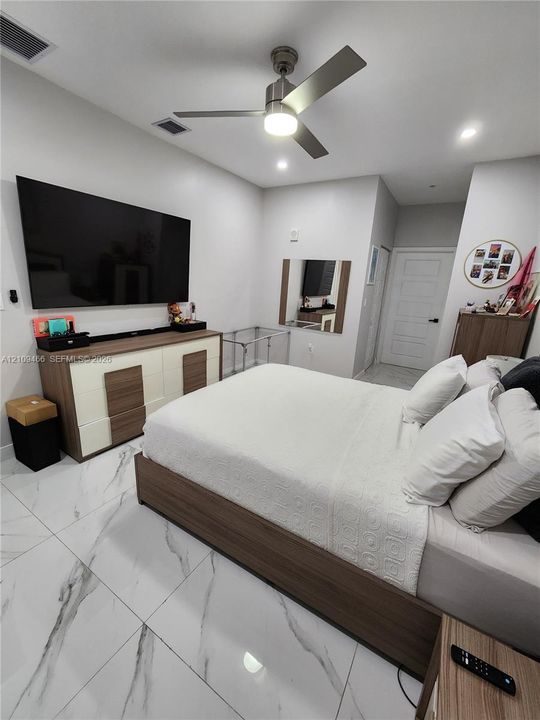 Large-format white tile flooring with veining, multi-speed brushed nickel ceiling fan with integrated lighting, and a multi-panel door