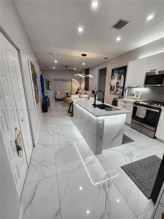 Kitchen featuring large-format veined tile flooring, center island with stone-finish waterfall edge, undermount sink with high-arc matte black faucet, and recessed ceiling lighting