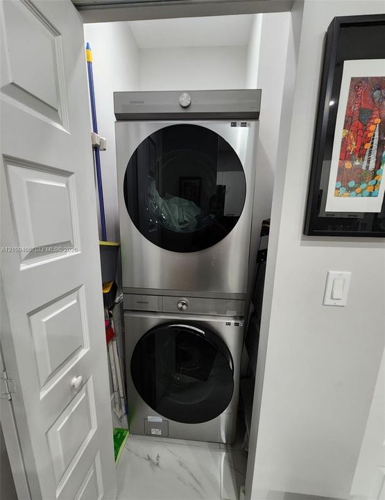 Stacked stainless steel laundry unit with circular front-loading doors and stone-finish flooring