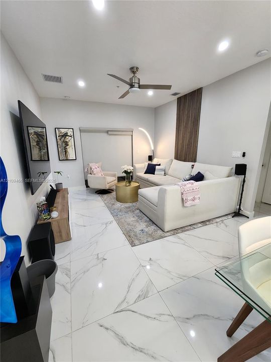 Large-format white stone-finish flooring, high ceilings with recessed lighting, brushed metal ceiling fan, and vertical wood-slat accent wall