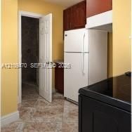 Kitchen featuring dark-toned cabinetry, a white refrigerator, black stovetop, and patterned tile flooring